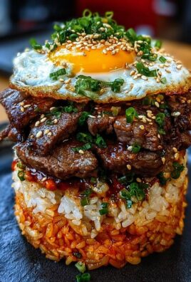 Stack of Korean BBQ beef over spicy rice topped with fried egg, green onions, and sesame seeds on a black plate